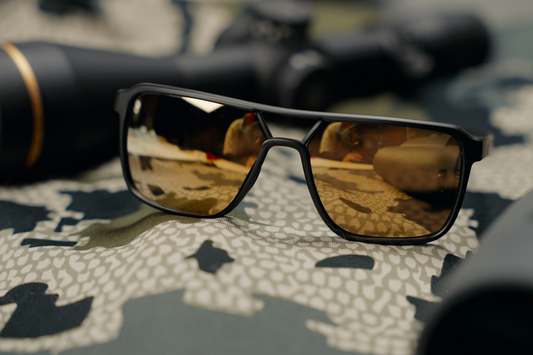 Sunglasses with brown mirrored lenses and black frame placed on a camo patterned fabric