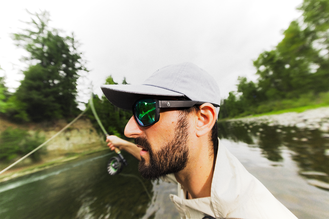 Side view of an angler fly fishing on a river in Revant Caster Sunglasses with Emerald Green lenses.