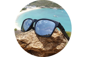 View of a frame with titanium lenses installed. The frame is sitting on a rock with a beach in the background.