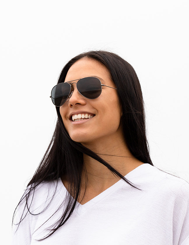 Shoulders-up view of a model with long, dark hair smiling and wearing sunglasses with Adapt gray photochromic lenses.