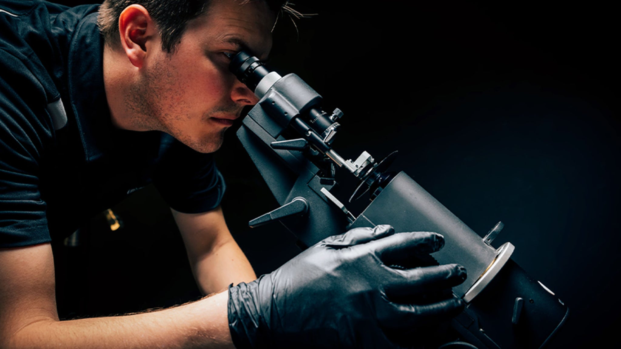 Man leaning down to look into a microscope with a sunglass lens sitting in front of it.