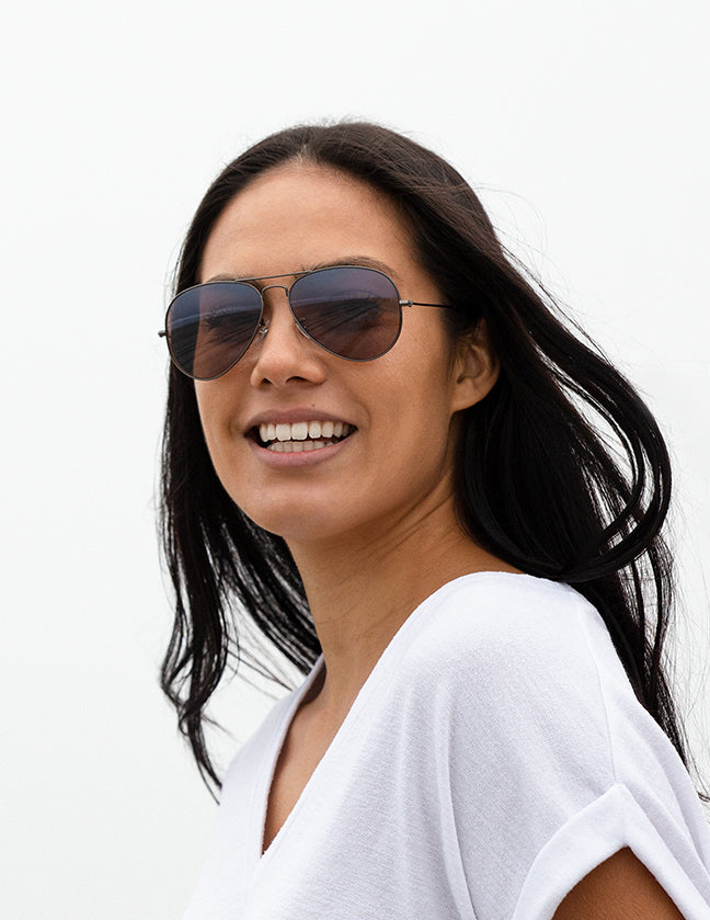 Shoulders-up view of a model with long, dark hair smiling and wearing sunglasses with Flash Bronze lenses.