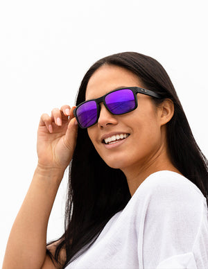 Shoulders-up view of a model with long, dark hair smiling and wearing sunglasses with Plasma Purple lenses