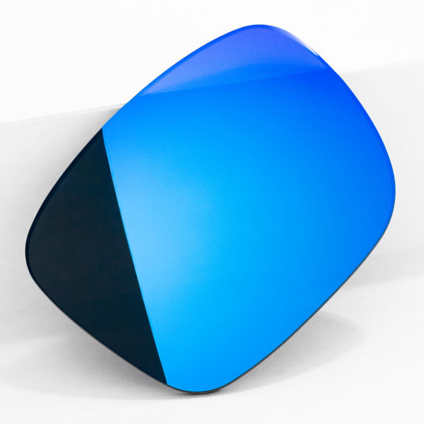 One Ice Blue sunglass lens with mirrorshield leaning on a white wall.