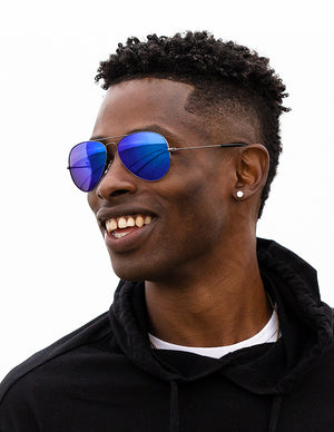 Shoulders-up view of a model with short, dark hair smiling and wearing sunglasses with Tidal Blue Lenses.